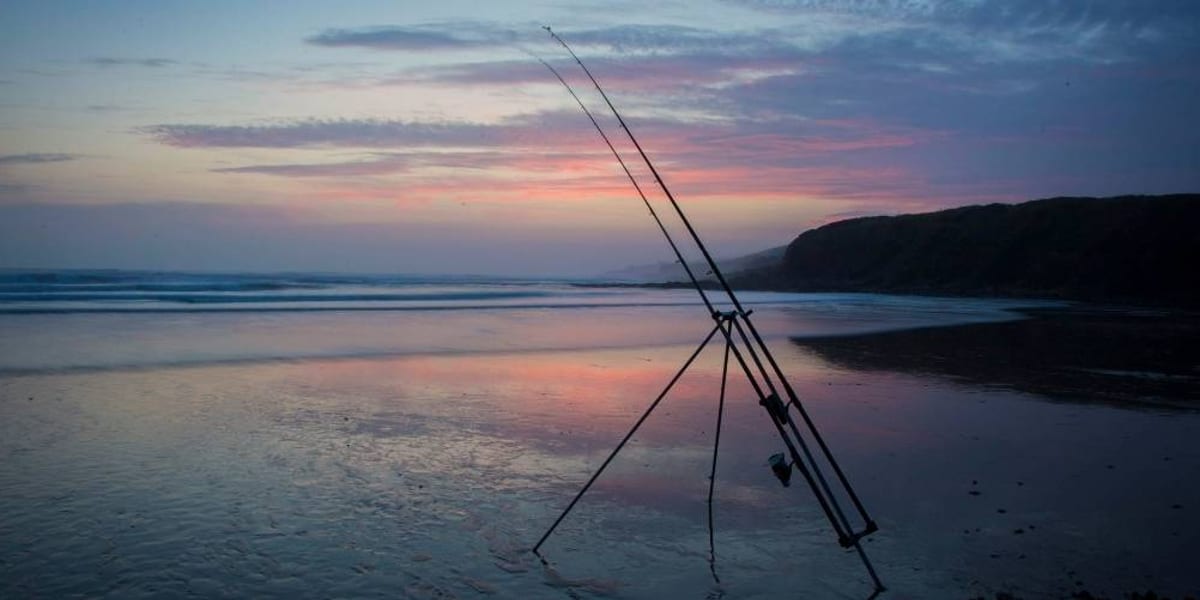 Sea fishing beach tripod holding two beachcaster rods on a shingle beach at sunset