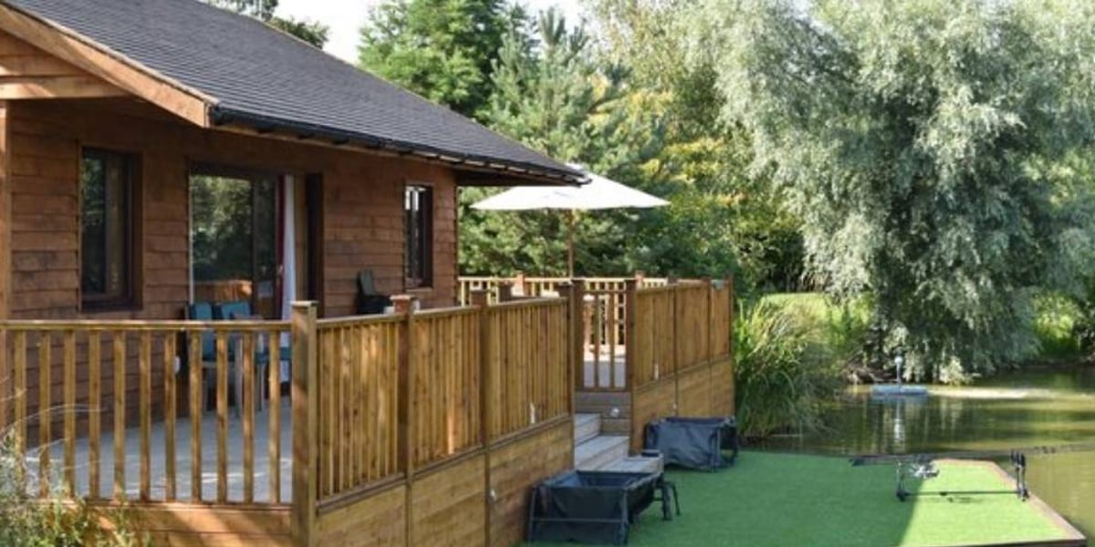 A wooden holiday lodge with decking overlooking a UK carp fishing lake